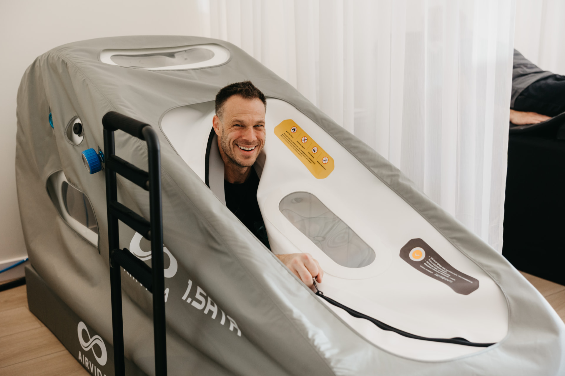 A smiling member sitting inside the Recharge hyperbaric oxygen chamber